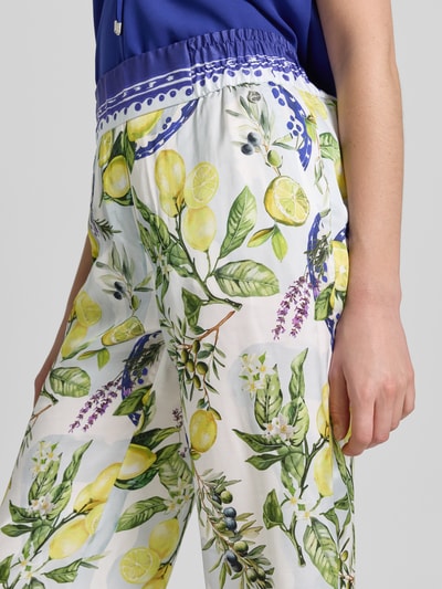 Kobiece modelka nosi Straight Fit Stoffhose aus reiner Viskose mit Allover-Motiv-Print von Marc Cain, biały kolor z nadrukiem cytryn i zielonych liści, częściowo elastyczny pas, szerokość w rozmiarze 36: 40 cm, długość wewnętrzna nogawki w rozmiarze 36: 64 cm, motyw na całej powierzchni, skrócony fason, wiskoza, detailaufnahme biodra i uda.