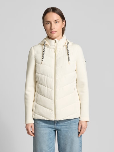 Modelka kobieca nosi Slim Fit Steppjacke mit gefüttertem Stehkragen von Christian Berg Woman Selection, kremowy kolor, krój slim fit, kaptur z kołnierzem, zamek błyskawiczny, kieszenie na zamek, długość pleców w rozmiarze 36: 60 cm, szerokość ramion w rozmiarze 36: 41 cm, szerokość klatki piersiowej w rozmiarze 36: 51 cm, długość rękawa w rozmiarze 36: 62 cm; widok całej sylwetki od przodu.