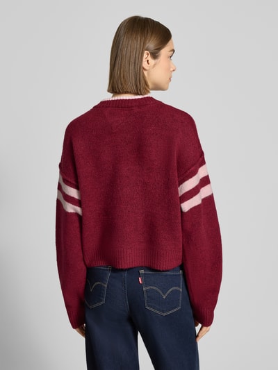 Männermodel trägt Oversized Strickpullover mit Woll-Anteil von Tommy Jeans, unifarbener Strick, Label-Stitching, gerippte Abschlüsse, Ganzkörperansicht Rückansicht.