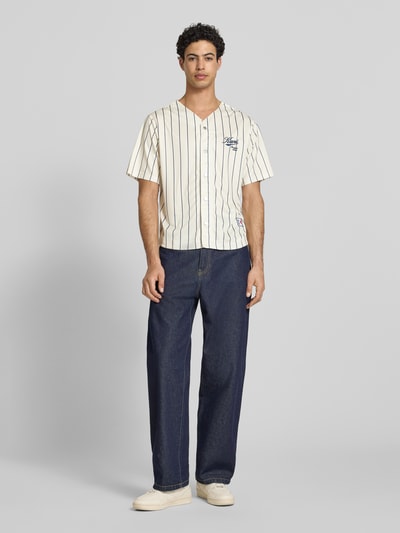 Männermodel trägt Regular Fit Freizeithemd mit Logo-Stitching von KARL KANI in Creme mit schwarzen Streifen, Knopfleiste, Ganzkörperansicht von vorne, Rückenlänge bei Größe M 64 cm, Schulterbreite 45 cm, Ärmellänge 27 cm, kurzärmeliges Design.