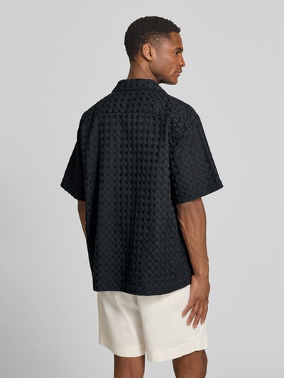 Männermodel trägt schwarzes Relaxed Fit Freizeithemd aus reiner Baumwolle Modell 'MONTY' von SELECTED HOMME, Jacquardtextur, Ganzkörperansicht Rückansicht.