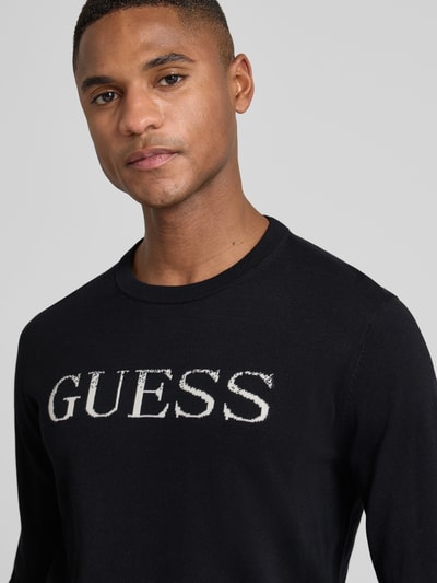 Männermodel trägt Regular Fit Pullover in Strick-Optik Modell 'Kane' von Guess, Baumwolle, Logo-Stitching, Nahaufnahme Oberkörper.