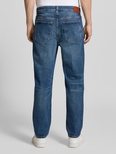 Männermodel trägt Tapered Fit Jeans aus Baumwoll-Mix Modell 'SONNY' von Tommy Jeans, stylizowana na denim, krój regular fit, krój tapered fit, naszywka z logo, nity, szlufki na pasek, zapięcie na guzik i ukryty zamek błyskawiczny, 5 kieszeni, mieszanka bawełny. Ganzkörperansicht Rückansicht.
