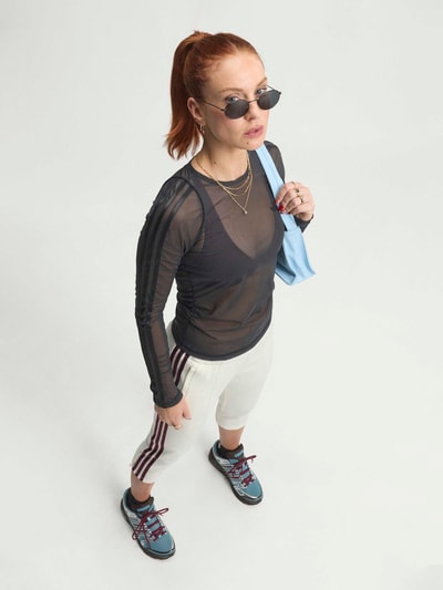 Vrouwenmodel draagt Regular Fit Sport-Langarmshirt met Logo-Detail van adidas Training, effen mat mesh met spitzenmotief, ronde hals, lange mouwen met rolzoom, logo-applicatie, detailopname bovenlichaam.