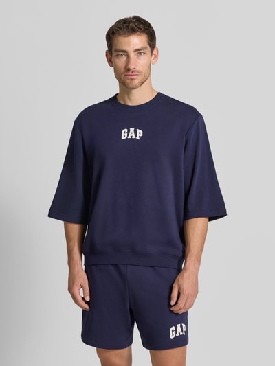 Männermodel trägt T-Shirt mit Rundhalsausschnitt und Logo-Print von GAP in Dunkelblau, Baumwoll-Mix, Loose Fit, Ganzkörperansicht von vorne.