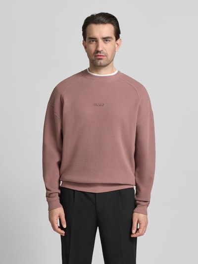 Männermodel trägt Regular Fit Sweatshirt aus reiner Baumwolle Modell 'DAFFLYN' von HUGO in Altrosa mit Strukturmuster, Ganzkörperansicht von vorne.