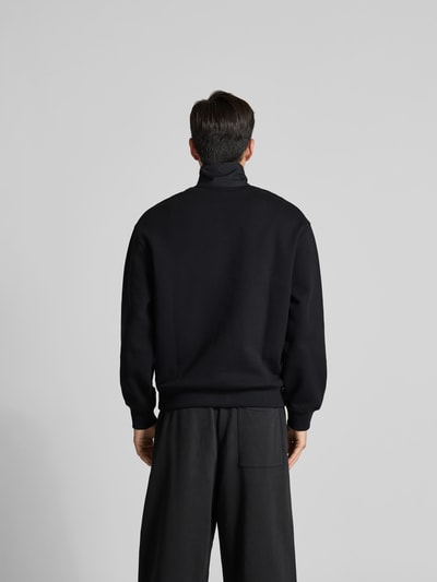 Mannenmodel draagt Troyer aus reiner Baumwolle van MAISON KITSUNÉ in zwart, regular fit, borstzak, labeldetail, ruglengte maat M 68 cm. Ganzkörperansicht Rückansicht.