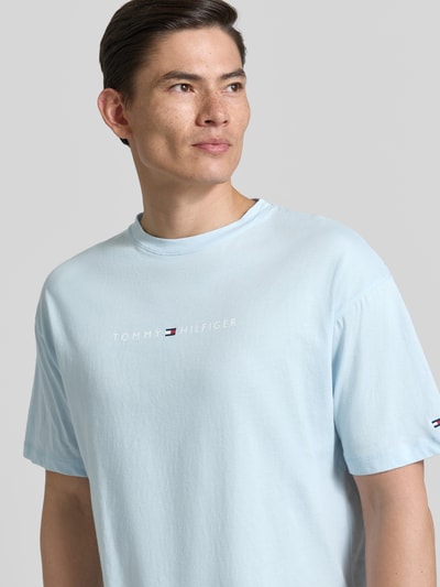 Męski model nosi Regular Fit T-Shirt mit Label-Schriftzug aus reiner Baumwolle von Tommy Hilfiger, jasnoniebieski, bawełna, unikolor, krój regular fit, napis z logo, okrągły dekolt, krótki rękaw. Nahaufnahme górnej części ciała.
