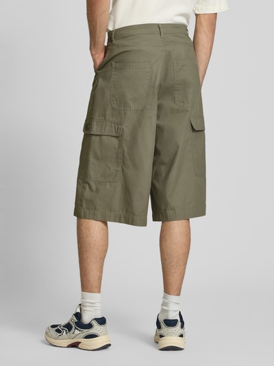 Mężczyzna nosi Straight Fit Shorts mit Cargo-Taschen Modell 'Camo' von KARL KANI z bawełny, wpuszczane kieszenie, kieszenie cargo, kieszenie z tyłu, zapięcie na guzik i zamek błyskawiczny, szerokość w rozmiarze M: 41 cm, długość wewnętrzna nogawki: 38 cm, kolor oliwkowy, widok całej sylwetki z tyłu.
