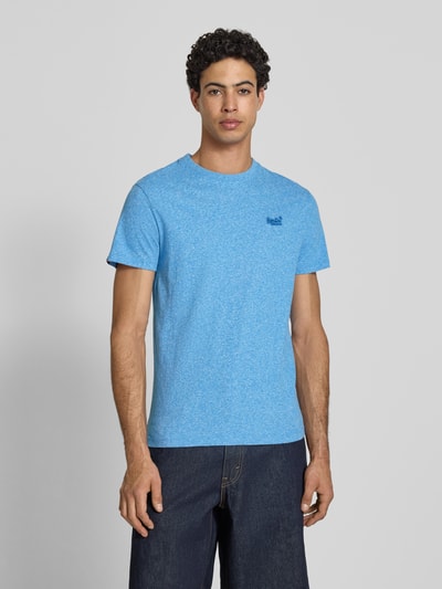 Männermodel trägt Regular Fit T-Shirt mit Logo-Stitching von Superdry in Hellblau aus reiner Baumwolle, Rundhalsausschnitt, Ganzkörperansicht von vorne. Rückenlänge bei Größe M: 69 cm.