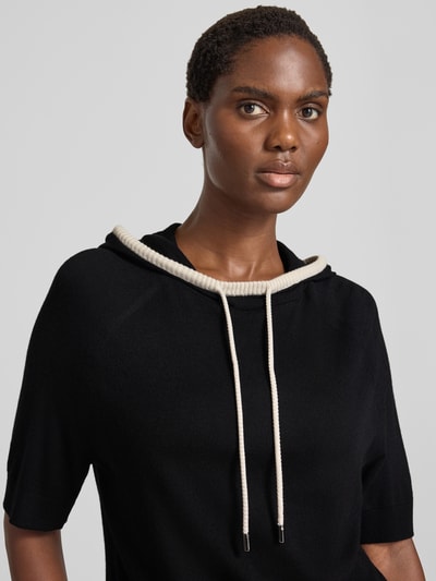 Frauenmodel trägt Relaxed Fit Hoodie aus Woll-Mix von Marc Cain in Schwarz mit Kontrast-Kordelzug, Strick-Optik, Nahaufnahme Oberkörper.