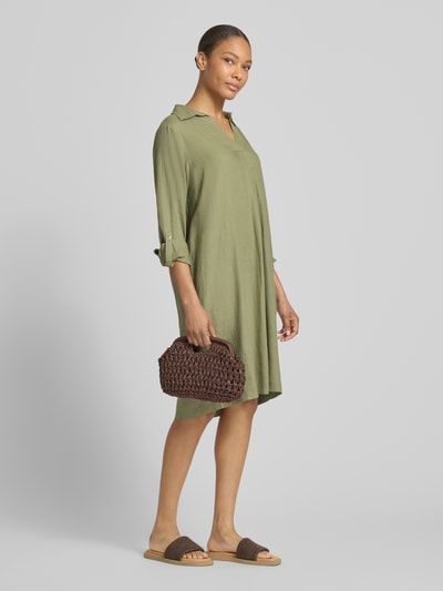 Frauenmodel trägt figurumspielendes Freizeitkleid aus Leinen-Viskose-Mix von s.Oliver RED LABEL, unifarbenes Midi-Kleid in Oliv, V-Ausschnitt, lange Ärmel mit Turn-up-Option, lockere Passform, Flammgarn-Struktur, Ganzkörperansicht von vorne.