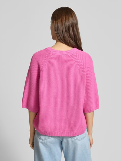 Frauenmodel trägt Oversized Strickpullover aus reiner Baumwolle Modell 'MARGE' von JJXX in Pink mit Strick-Optik, 3/4-Arm, gerippte Abschlüsse, Ganzkörperansicht Rückansicht.