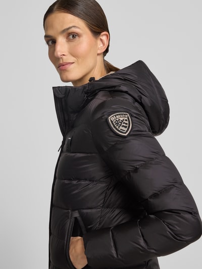 Kobiece model nosi kurtkę puchową z efektem pikowania, detal z logo, kaptur, krój taliowany, Model 'Charme' od Blauer USA, czarna, długość tyłu w rozmiarze S: 62 cm, szerokość ramion w rozmiarze S: 44 cm, szerokość w rozmiarze S: 43 cm, długość rękawów w rozmiarze S: 62 cm, zamek błyskawiczny dwustronny, zbliżenie na górną część ciała z przodu.