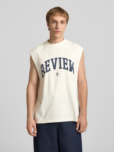 Männermodel trägt Tanktop mit Logo-Print von REVIEW in Creme mit geradem Schnitt, Rundhalsausschnitt, reine Baumwolle, Ganzkörperansicht von vorne.