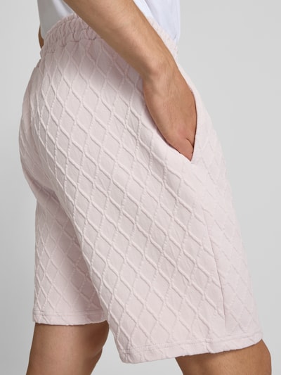 Männermodel trägt Relaxed Fit Sweatshorts mit Strukturmuster Modell 'Jovren' von Pegador in Hellrosa, Detailaufnahme Schrägansicht. Elastischer Material-Mix mit Baumwoll-Anteil, Strukturmuster, Bundweite bei Größe M: 39 cm, Innenbeinlänge bei Größe M: 24 cm.