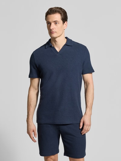 Męski model nosi Regular Fit Poloshirt aus Baumwoll-Mix von MCNEAL, mieszanka bawełny i elastanu, kratka pika, wykładany kołnierz, dekolt w serek, krótki rękaw, długość tyłu w rozmiarze M: 69 cm, ciemnoniebieski kolor, pełny przód, tekstura waflowa, gładka powierzchnia, całopostaciowy widok z przodu.