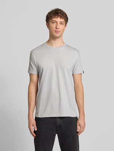 Męski model nosi T-Shirt mit Label-Print und Rundhalsausschnitt von Alpha Industries, szary, bawełna, krój regular fit, długość tyłu w rozmiarze M: 67 cm, widok całej sylwetki z przodu.