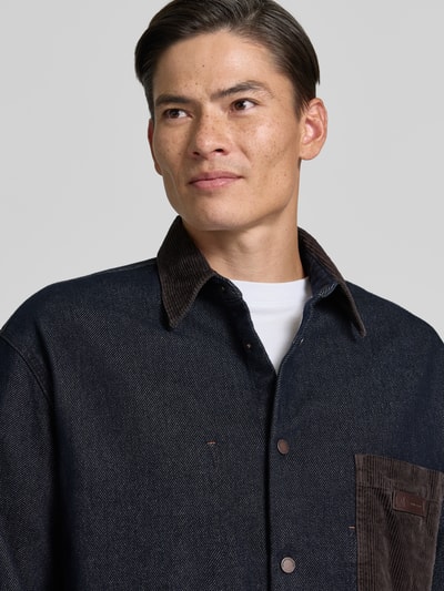 Männermodel trägt Overshirt mit Kentkragen in Cord-Optik und Label-Patch von Armani Exchange, dunkelblau und braun, Nahaufnahme Oberkörper, regular fit, met borstzak, sportmanchetten, ruglengte maat M 70 cm.