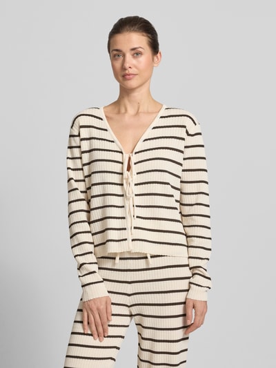 Kobiece model prezentuje Loose Fit Cardigan aus Viskose-Mix Modell 'NURIA' von VILLA SOPHIE, efekt: wzór na całej powierzchni, krój loose fit, taśma do wiązania, dekolt w serek, aplikacja z metką, rękawy długi rękaw, wykończenie materiału: dzianina, mieszanka wiskozy, kolor kremowy z czarnymi paskami, całkowity widok z przodu.