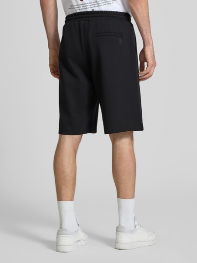 Männermodel trägt Shorts mit elastischem Bund und Ziernähten von REVIEW in Schwarz, Material-Mix mit Stretch-Anteil, Loose-Fit, Ganzkörperansicht Rückansicht.