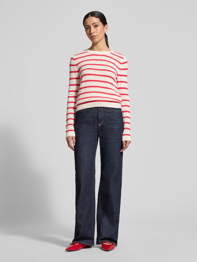 Frauenmodel trägt Strickpullover mit Rundhalsausschnitt Modell 'DALO' von Vila aus reiner Baumwolle, Slim-Fit, rot-weiß gestreift, Ganzkörperansicht von vorne.