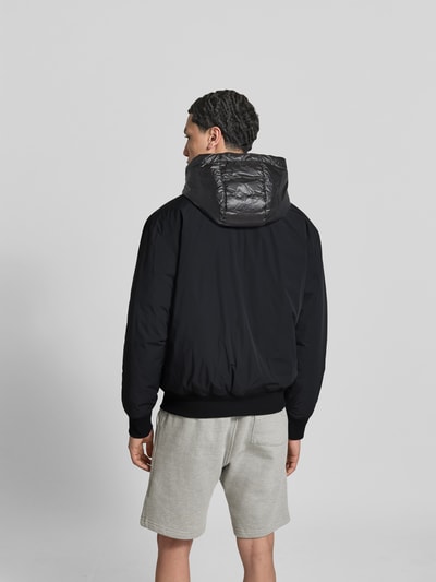 Männermodel trägt Bomberjacke mit Daunen-Feder-Füllung von Moose Knuckles in Schwarz mit Kapuze, lockerer Passform, Rückansicht, Rückenlänge 63 cm.