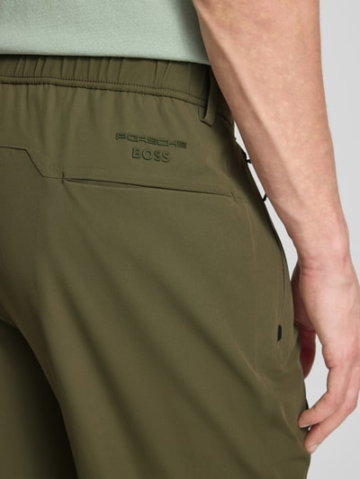 Männermodel trägt Regular Fit broek met persplooien model 'PS SPIRIT70' van BOSS Green X PORSCHE, look: effen, stretch, labelopschrift, detailopname rug.