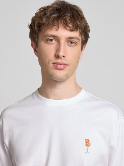 Männermodel trägt Relaxed Fit T-Shirt aus reiner Baumwolle Modell 'FRED' von Only & Sons, weiß, Label Patch, Motiv-Stitching, Nahaufnahme Oberkörper.