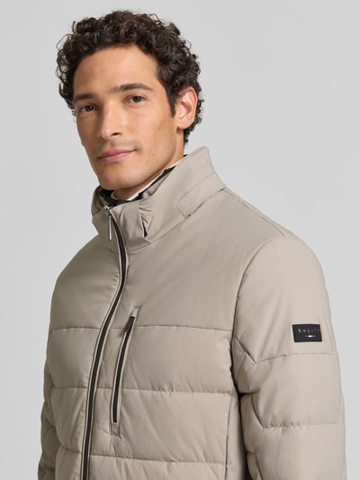 Männermodel trägt Steppjacke mit Zweiwege-Reißverschluss von bugatti in Beige, glatte Struktur, krój regular fit, Nahaufnahme Oberkörper. Szerokość w rozmiarze 50: 60 cm, długość tyłu: 75 cm, szerokość ramion: 49 cm, długość rękawa: 67 cm, kaptur z troczkiem, kieszenie na zamek.