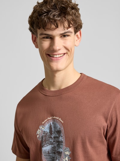 Mannelijk model draagt T-shirt met Label-Print model 'NIAGARA' van Jack & Jones, bruine katoen, rechte fit, ronde hals, labelprint, close-up bovenlichaam.