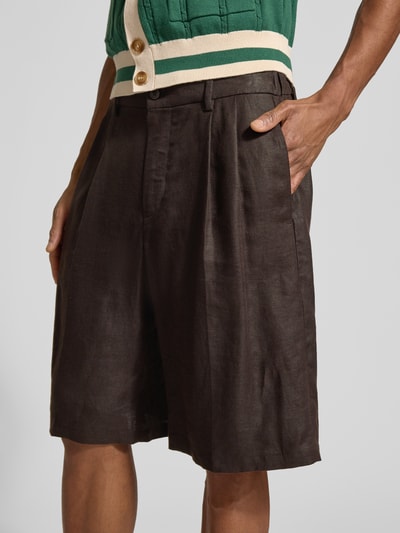 Mężczyzna nosi Leinenshorts aus reinen Leinen od Drykorn, ciemnobrązowy kolor, luźny krój, kieszenie, szerokość w rozmiarze 33: 44 cm, długość wewnętrzna 25 cm, zbliżenie na górną część nóg i biodra.