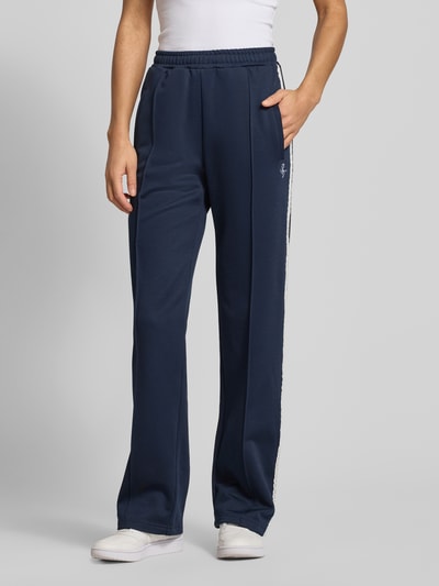 Frauenmodel trägt Sportliche Trackhose mit geradem Bein von REVIEW, granatowy kolor, prosty krój, koronkowe elementy przy bocznym szwie, zaszewka z przodu, wyhaftowane logo na bocznej kieszeni, długość wewnętrzna nogawki w rozmiarze S: 39 cm, przód w pełnej długości, Ganzkörperansicht von vorne.