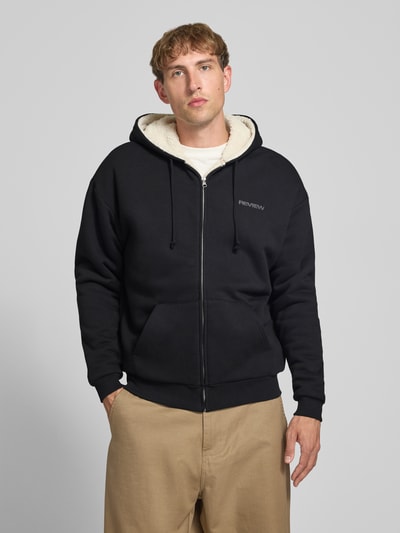 Männermodel trägt Regular Fit Sweatjacke aus Baumwoll-Mix mit Teddyfutter von REVIEW in Schwarz, Logo-Detail, Nahaufnahme Oberkörper.