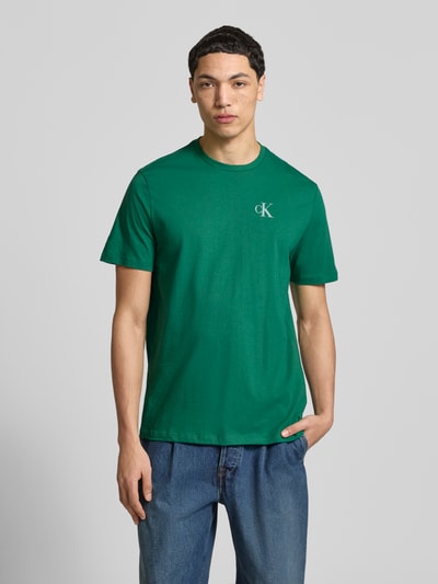 Männermodel trägt Regular Fit T-Shirt mit Logo-Print von Calvin Klein Jeans in Grün aus reiner Baumwolle, Rundhalsausschnitt, Ganzkörperansicht von vorne. Rückenlänge bei Größe M: 68 cm.