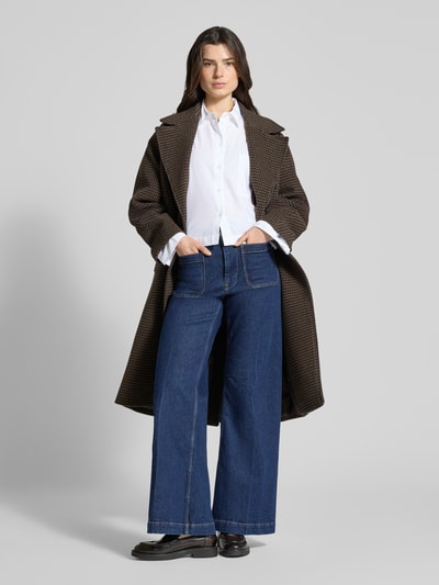 Frauenmodel trägt Oversized Hemdbluse aus reiner Bio-Baumwolle Modell 'Astha' von Selected Femme in Weiß, kombiniert zu Jeans und Mantel, unifarbene Optik, Webware, Ganzkörperansicht von vorne.