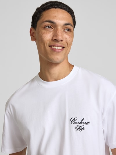 Männermodel trägt T-Shirt mit Logo-Stitching Modell 'Gracious' von Carhartt Work In Progress in Weiß, Nahaufnahme Oberkörper, reine Baumwolle, Relaxed Fit, Rundhalsausschnitt.