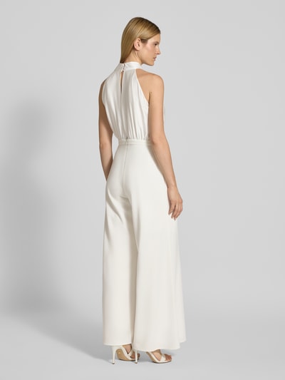 Vrouwenmodel draagt 'Jumpsuit met Strikapplicatie' van SWING in wit, getailleerd model, wijde benen, Halter, cut-out op de rug, ruglengte maat 36: 150 cm, borstwijdte maat 36: 36 cm, totale lengte maat 36: 155 cm, binnenbeenlengte maat 36: 80 cm. Volledige lichaamsweergave achteraan.
