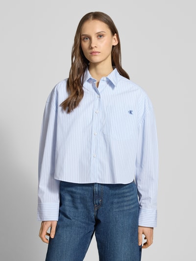Vrouwenmodel draagt 'Cropped Bluse mit Brusttasche und Label-Stitching' van Calvin Klein Jeans, blauw-wit gestreept katoen, borstzak, label-stitching, hemdenkraag, cropped fit, vooraanzicht bovenlichaam.