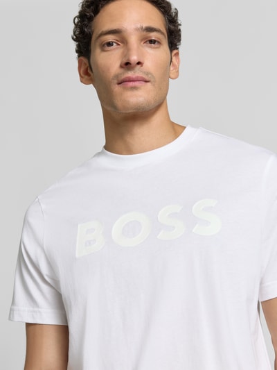 Mężczyzna nosi biały t-shirt krój regular fit Regular Fit T-Shirt aus reiner Baumwolle Modell 'TS_STRUCTURE LOGO 1027473' von BOSS Green, gładka struktura, logo z przodu, zbliżenie na górną część ciała.