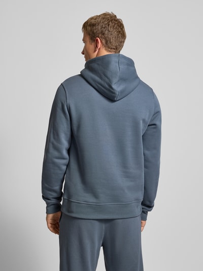 Męskimodel nosi Hoodie mit Kapuze von CHAMPION z mieszanki bawełny, luźny krój, kaptur, tunel, kieszeń kangurka, prążkowane wykończenia, wyhaftowane logo, długość tyłu 70 cm, długość rękawów 70 cm, widok całej sylwetki z tyłu.