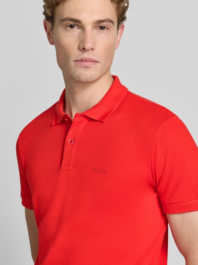 Mężczyzna nosi koszulkę polo Regular Fit Poloshirt aus reiner Baumwolle model 'PIO 1' od BOSS Green w kolorze czerwonym, widok z przodu, zbliżenie na górną część ciała.