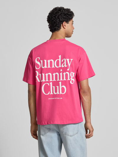 Männermodel trägt pinkes T-Shirt mit weißem Statement-Print, Modell 'Sunday Running Club' von ANOTHER COTTON LAB, Boxy Fit, Rückansicht.