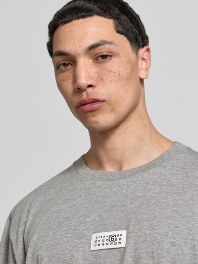 Männermodel trägt Oversized T-Shirt mit Logo-Detail von MM6 Maison Margiela in Grau, aus reiner Baumwolle, Nahaufnahme Oberkörper.