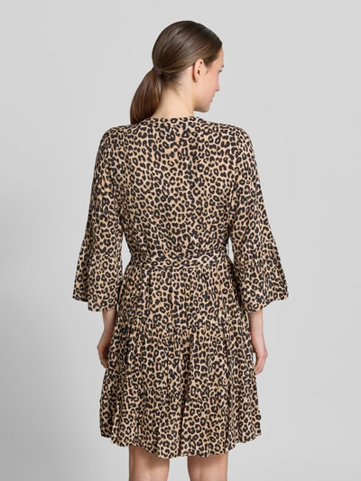 Vrouwenmodel draagt Tailliertes Tunikakleid aus reiner Viskose Modell 'MELBA' van Vero Moda met all-over print, getailleerde fit, mini lengte, v-hals, ceintuur en trompetmouwen, lichte en gladde stof, achterkant volledig zichtbaar, volledige lichaamsweergave achteraan.