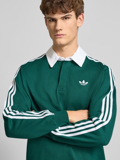 Männermodel trägt Poloshirt mit kurzer Knopfleiste von adidas Originals in Grün mit weißen Streifen, reine Baumwolle, Nahaufnahme Oberkörper.