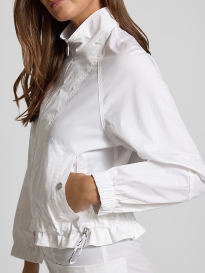 Frauenmodel trägt Regular Fit Jacke mit Stehkragen von Marc Cain in Weiß, Baumwoll-Mix, Druckknopfverschluss, Zweiwege-Reißverschluss, Tunnelzug im Bund, elastische Ärmelabschlüsse, Eingrifftaschen, Detailaufnahme Oberkörper. Rückenlänge bei Größe 36: 54 cm, Schulterbreite: 40 cm, Brustweite: 60 cm, Ärmellänge: 72 cm.