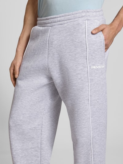 Männermodel trägt Sweatpants mit elastischem Bund und Logo von REVIEW in Hellgrau aus Reine Baumwolle, Relaxed-Fit, Nahaufnahme Oberschenkel.