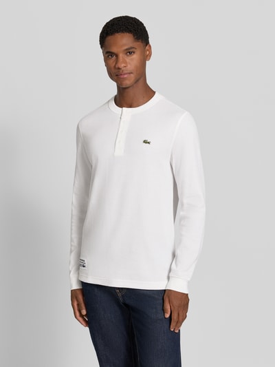 Männermodel trägt Regular Fit Langarmshirt aus reiner Baumwolle von Lacoste in Weiß, strukturierte Oberfläche, Ganzkörperansicht von vorne. Herren Langarmshirt von Lacoste