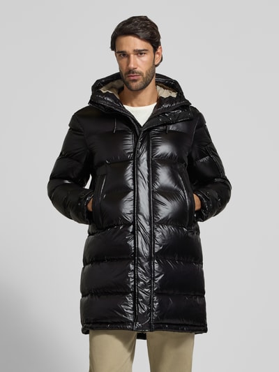 Männermodel trägt schwarze Steppjacke mit Kapuze und Eingrifftaschen Modell 'ALDRICH' von Blauer USA, glänzende Oberfläche, Ganzkörperansicht von vorne. Regular Fit, Label-Detail, Tunnelzug, Rückenlänge 94 cm, Schulterbreite 43 cm, Brustweite 61 cm, Ärmellänge 65 cm.